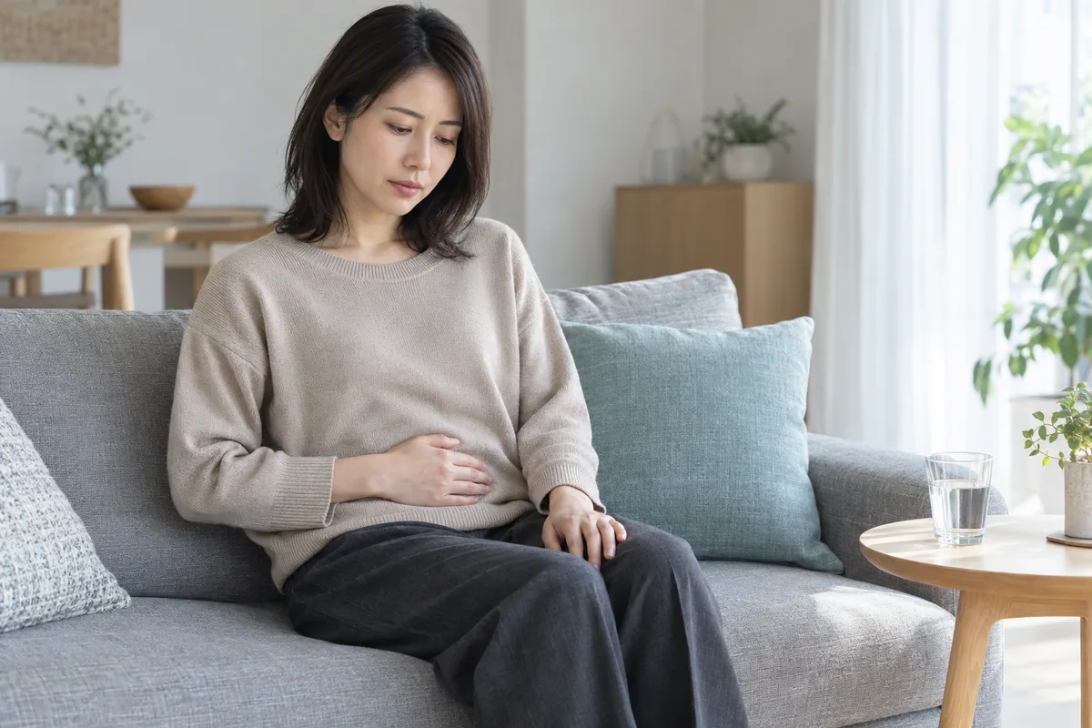 ソファでお腹に手を当てて休む女性