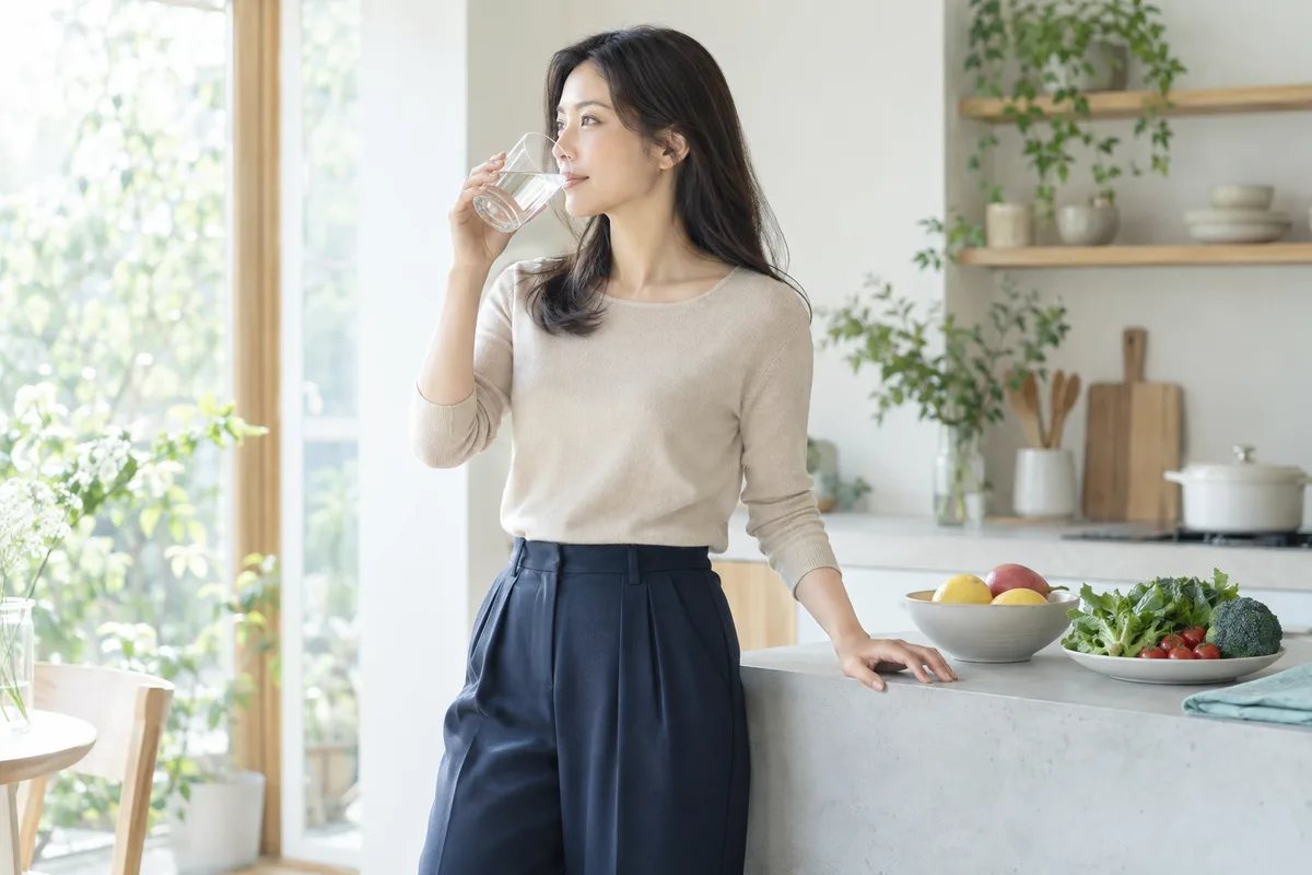 朝、キッチンで水を飲む女性